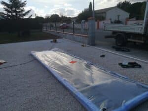 Installation de bâche/panneau solaire sur gravier blanc devant une clôture, avec camion de 'Création • Entretien de parcs & jardins'.